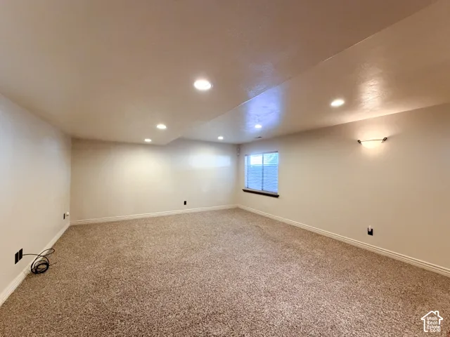 Expansive carpeted area featuring recessed lighting, a window with blinds, and a wall sconce