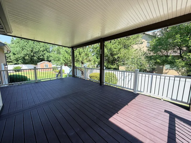 Expansive covered deck featuring composite decking in contrasting finishes, aluminum railings with horizontal balusters, and a solid roof structure providing all-weather outdoor living space