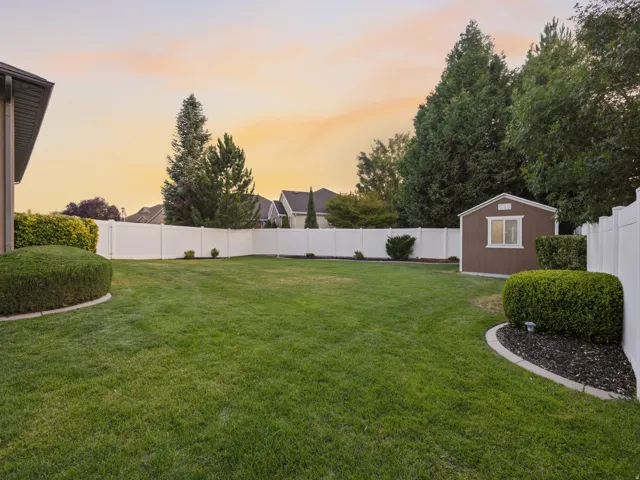 Spacious lawn area featuring a privacy fence, mature perimeter trees, and a functional storage shed