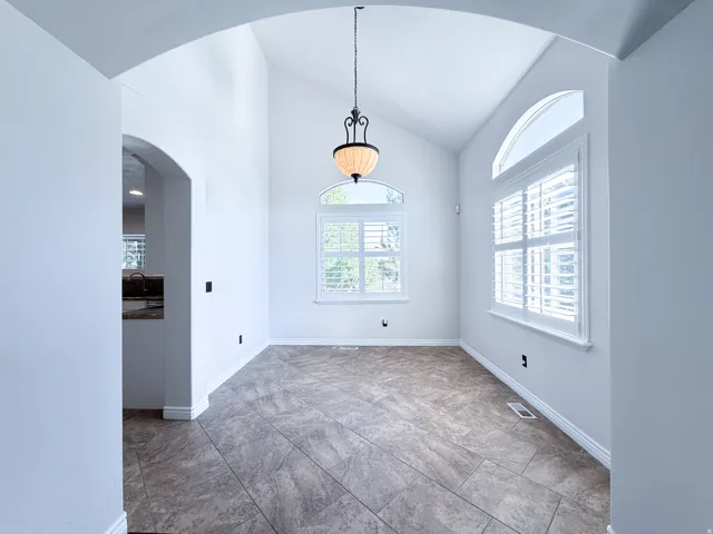 Arched entryway leading to a room with high vaulted ceilings, large windows with shutters, and a prominent hanging light fixture