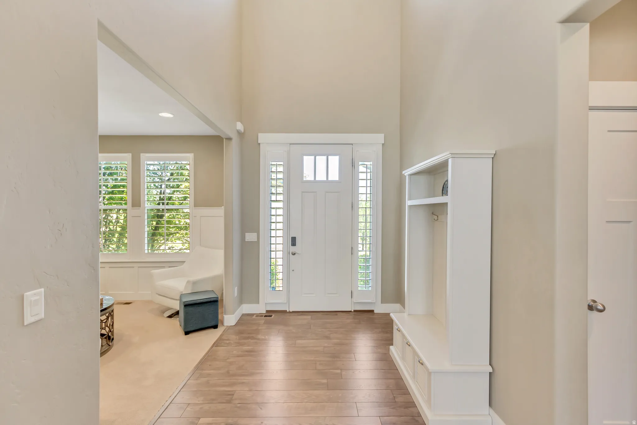 Two-story foyer with wood-finish flooring, a white paneled entry door with sidelights, and a built-in mudroom bench with storage and hooks