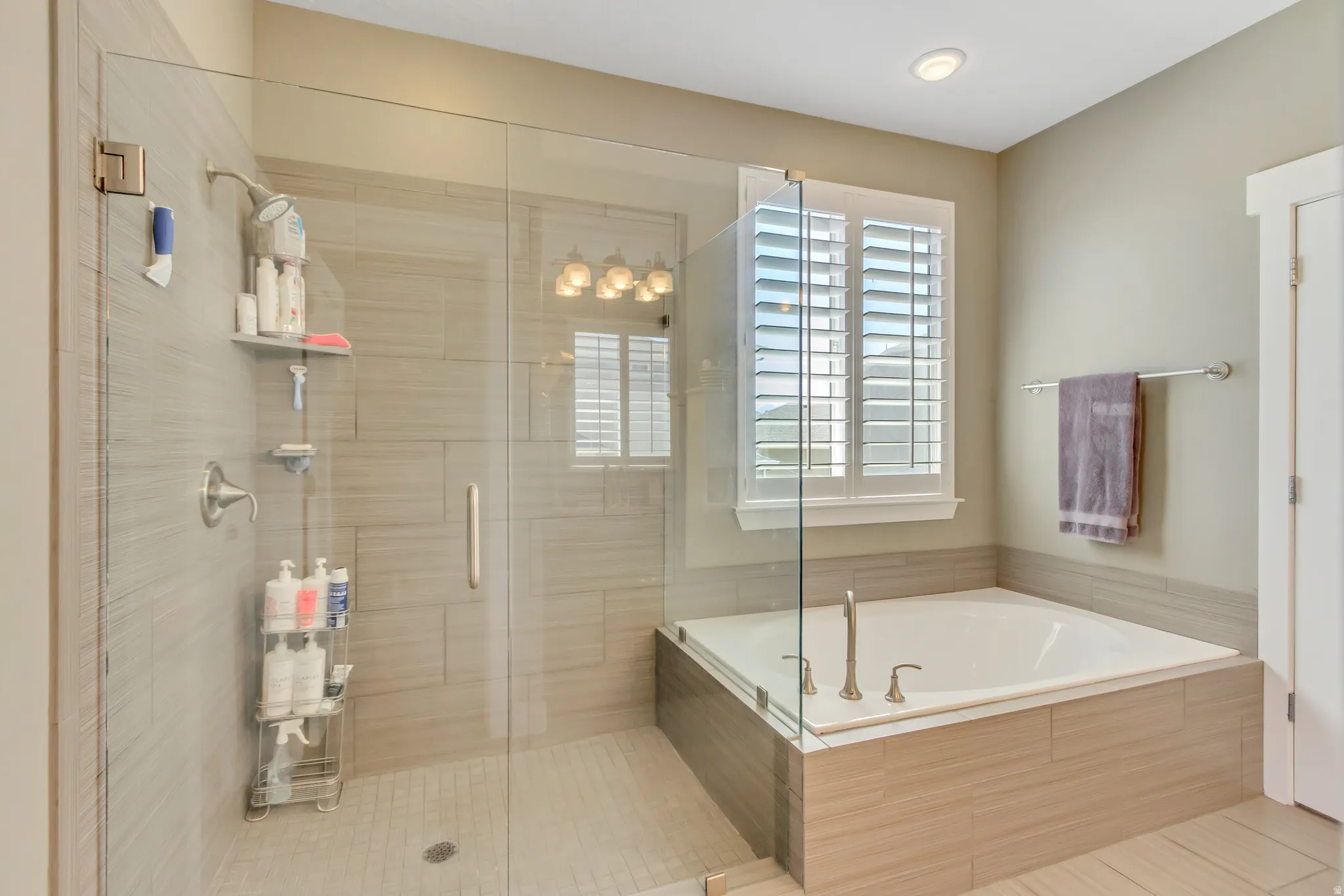 Contemporary bathroom featuring a glass-enclosed shower with tile surround, an inset soaking tub with a tiled base, and a window with plantation shutters