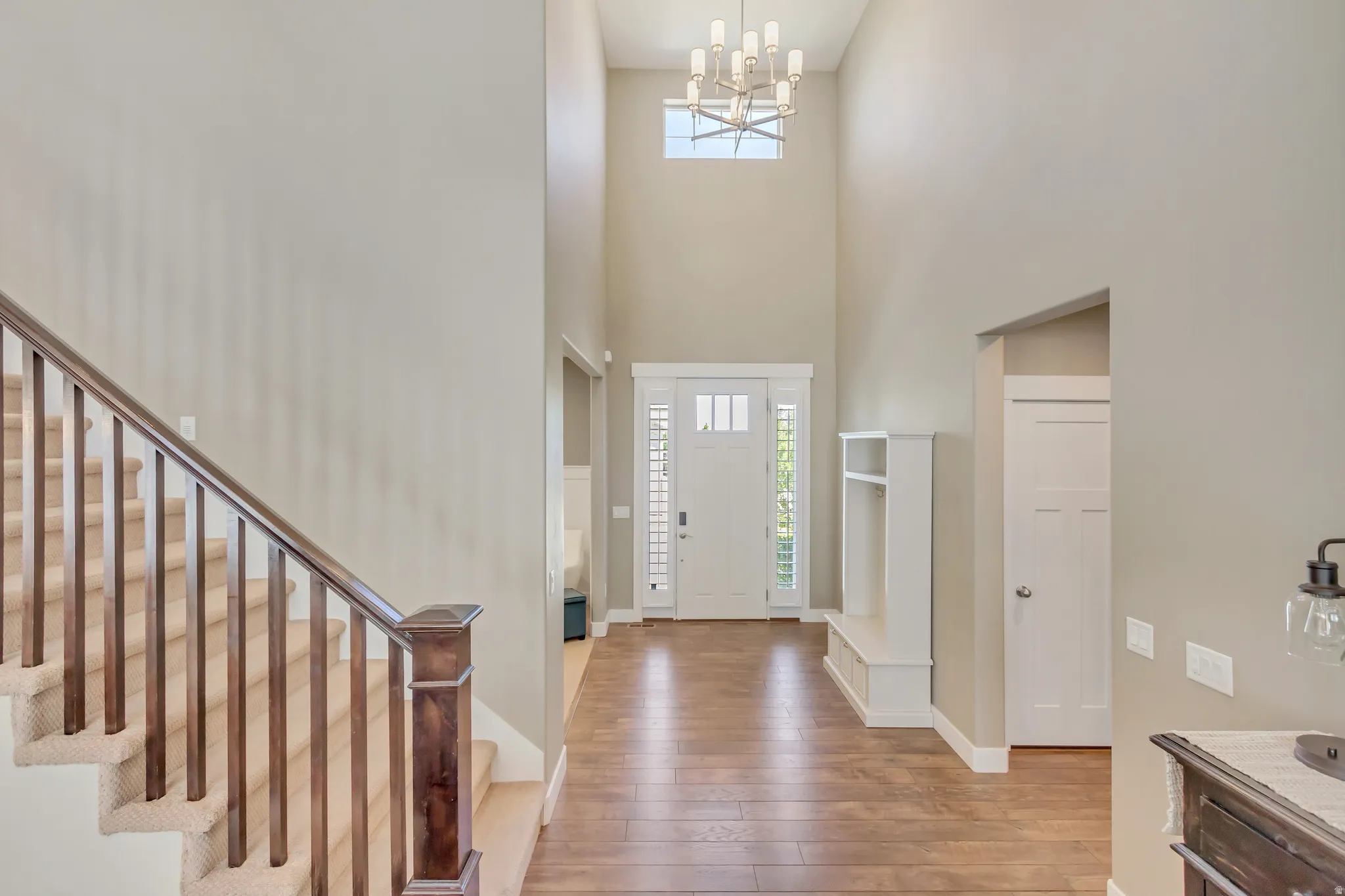 Entryway featuring soaring ceilings, wood-finish flooring, a built-in bench with storage, a contemporary chandelier, and a staircase with wood newel posts and carpeted treads