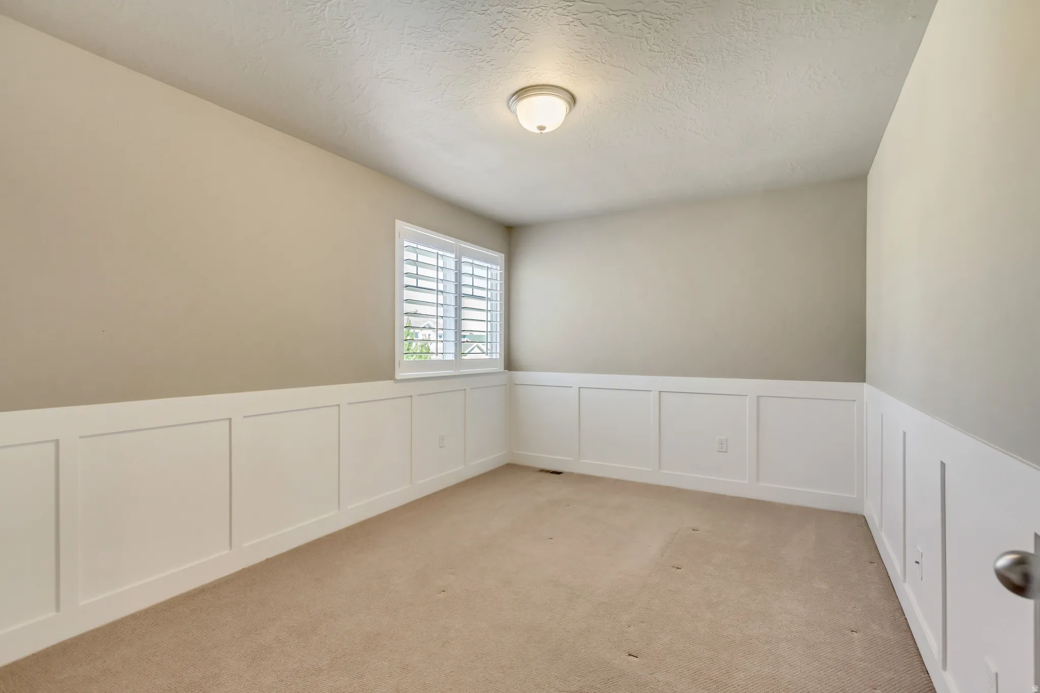 Interior room featuring neutral wall paint, white board and batten wainscoting, and a single window with white plantation shutters