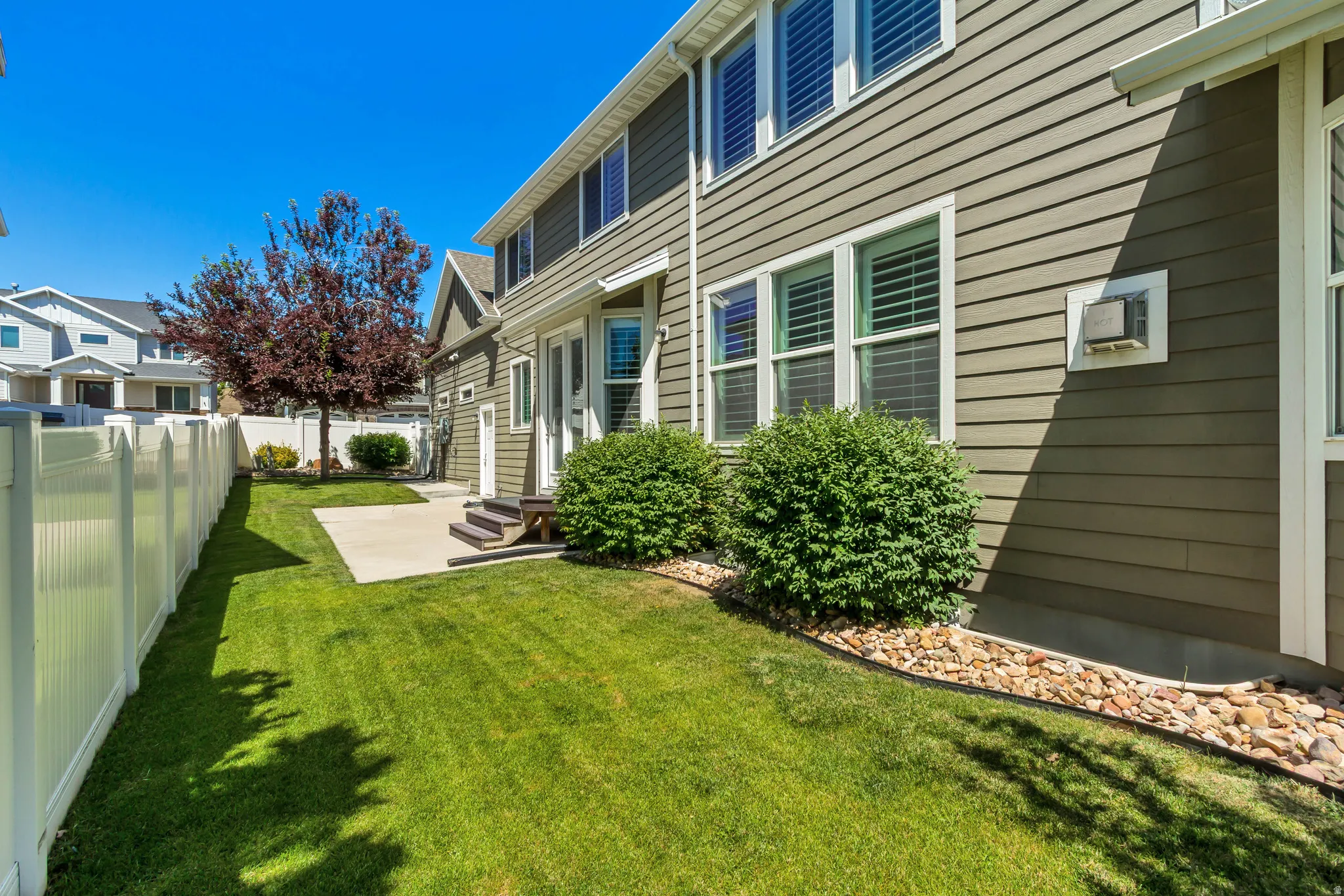 Expansive side yard featuring a manicured lawn, concrete patio, and mature landscaping