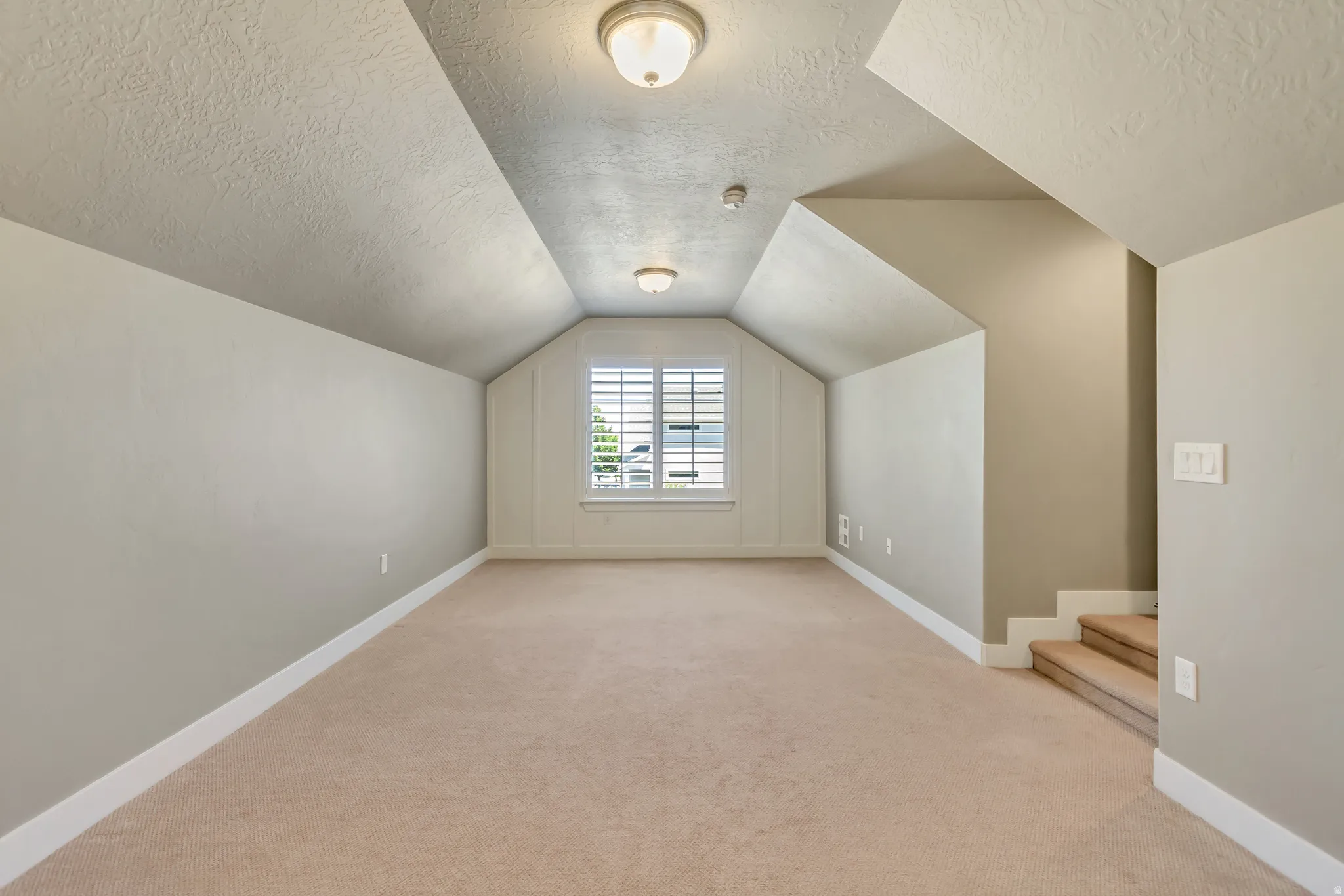 Carpeted room featuring a window with plantation shutters, sloped ceilings, recessed lighting, and a neutral color palette