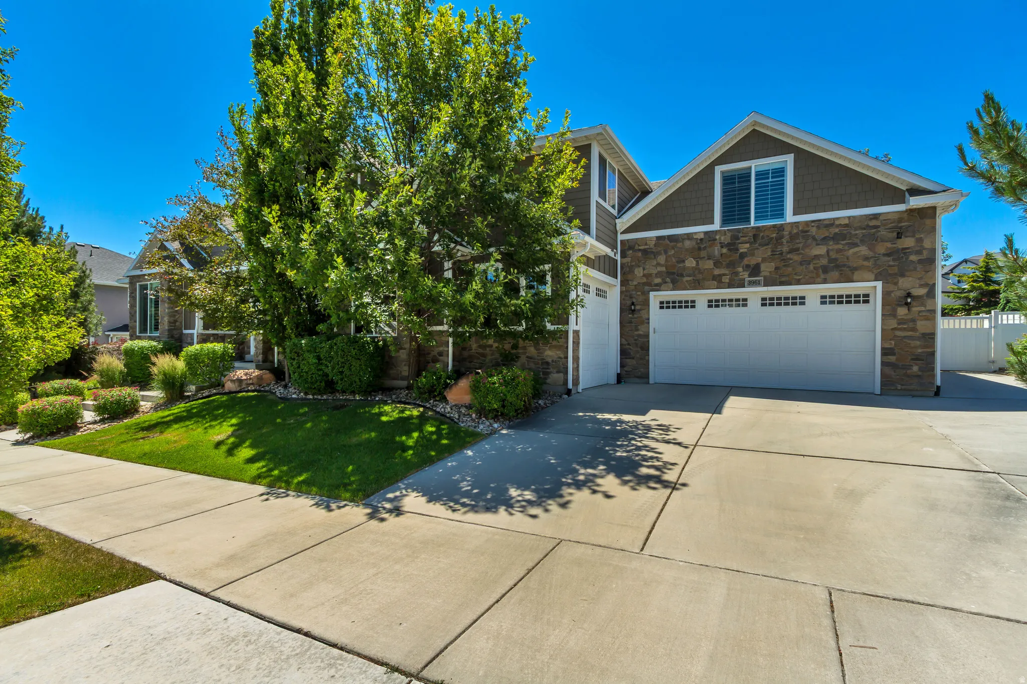 Two-story residence featuring stone and siding facade, an expansive concrete driveway, and attached two-car garage with overhead doors