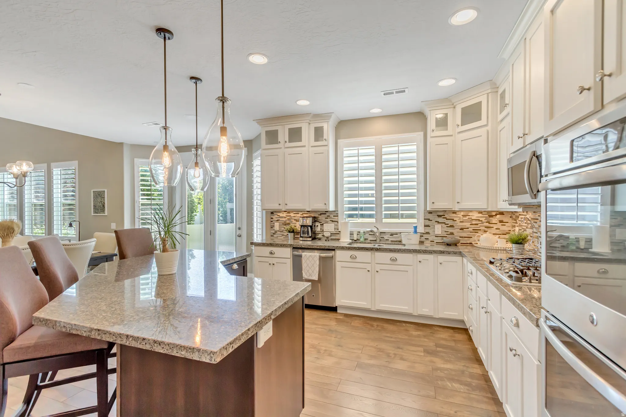 Kitchen featuring an expansive island with a granite countertop, white cabinetry with upper glass-front accents, and stainless steel appliances