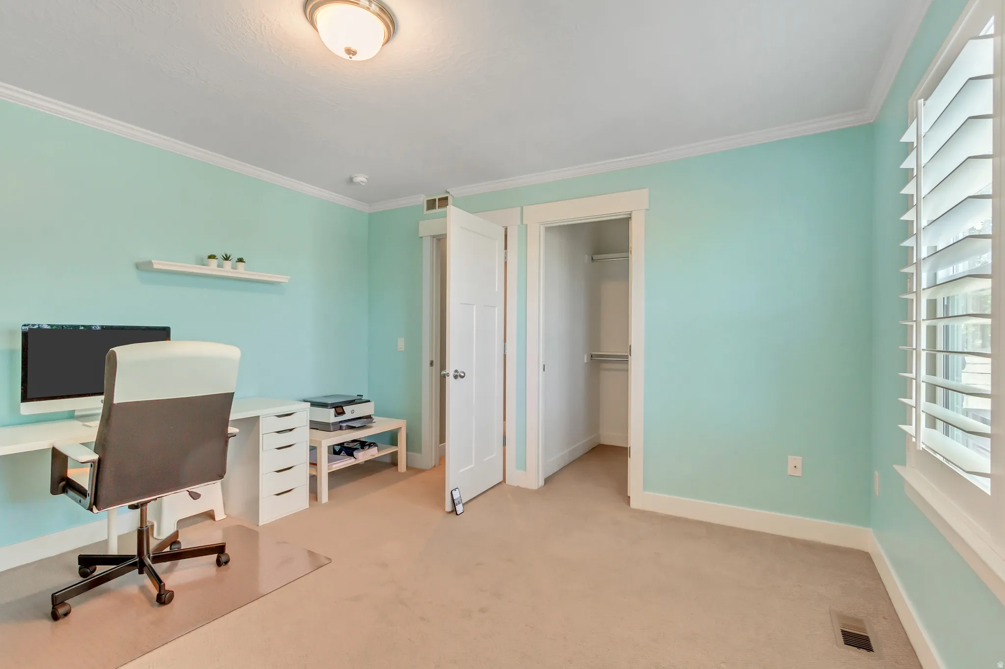 Carpeted room featuring a white floating shelf, crown molding, a flush mount ceiling light, and a window with white plantation shutters