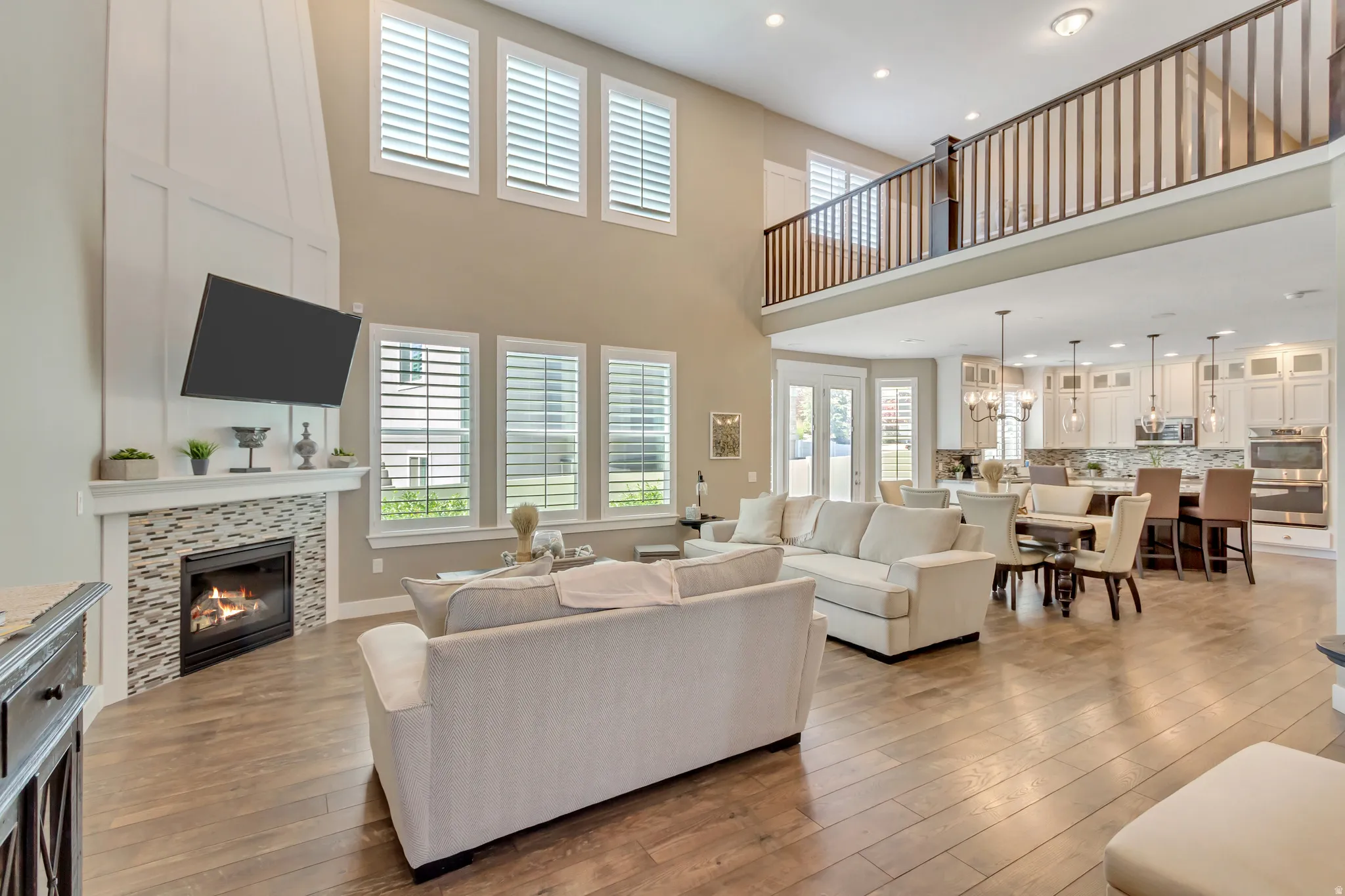 Spacious living area featuring high ceilings, wood-finish flooring, a contemporary fireplace with a tile surround, and multiple windows with plantation shutters