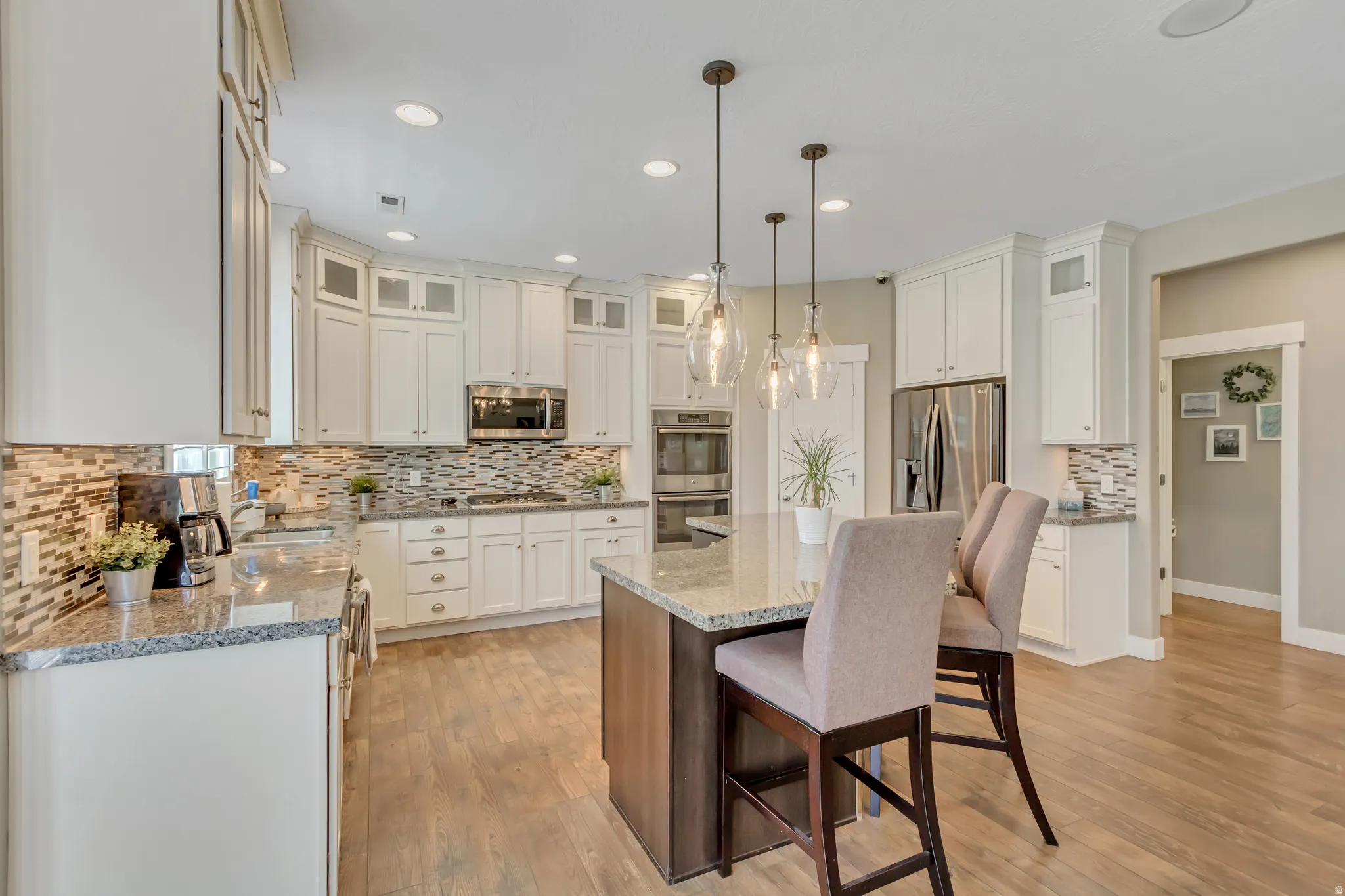 Expansive kitchen featuring white cabinetry, stainless steel appliances, a center island with pendant lighting, stone countertops, and wood-finish flooring