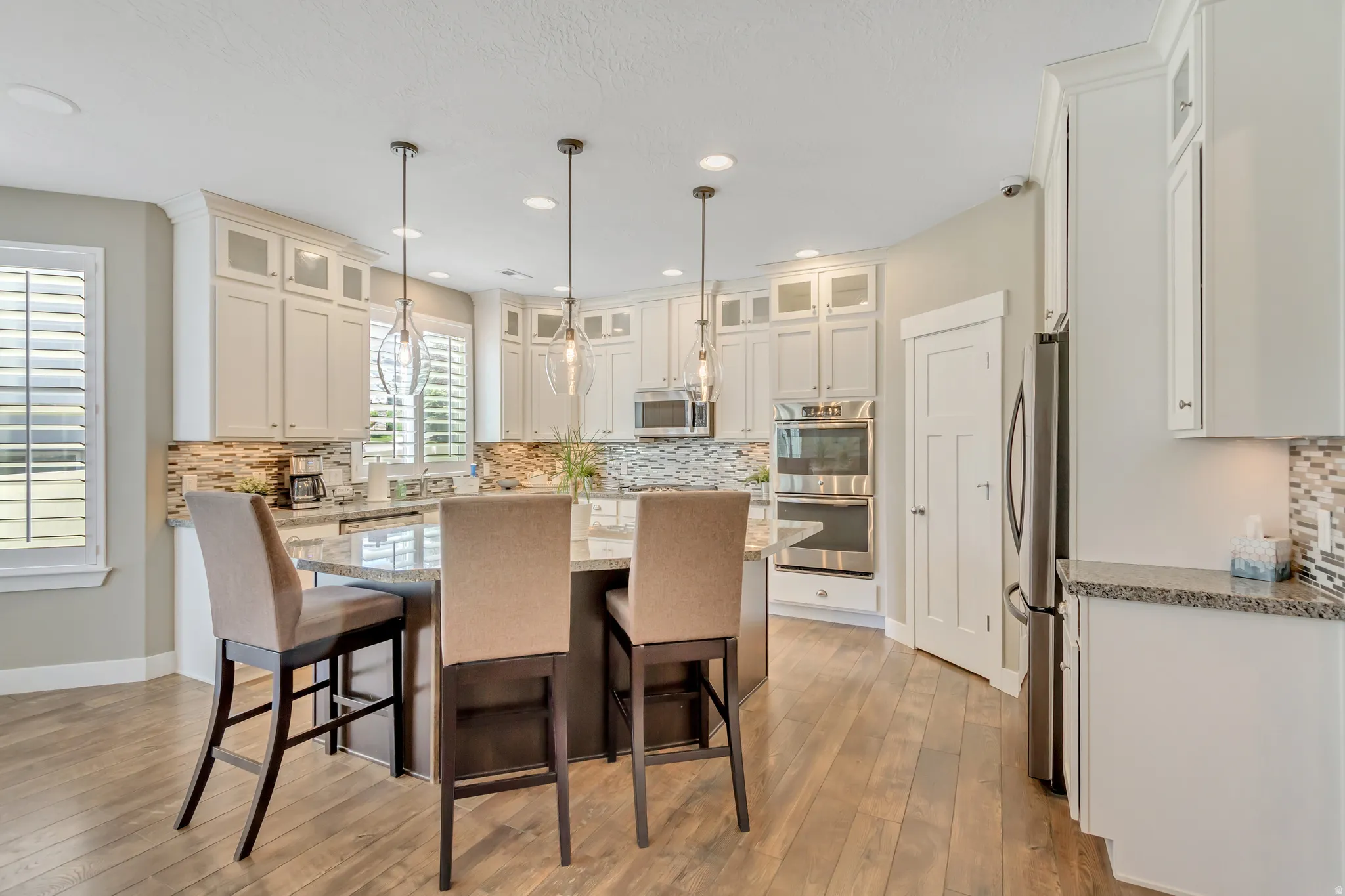 Open-concept kitchen featuring light-toned cabinetry, a multi-tone tile backsplash, and a central island with a stone countertop