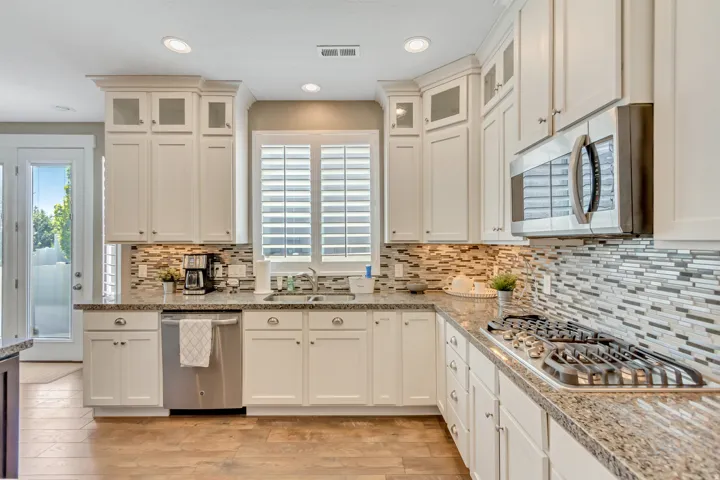 Kitchen featuring white cabinetry with glass inserts, stainless steel appliances, granite countertops, and a mosaic tile backsplash