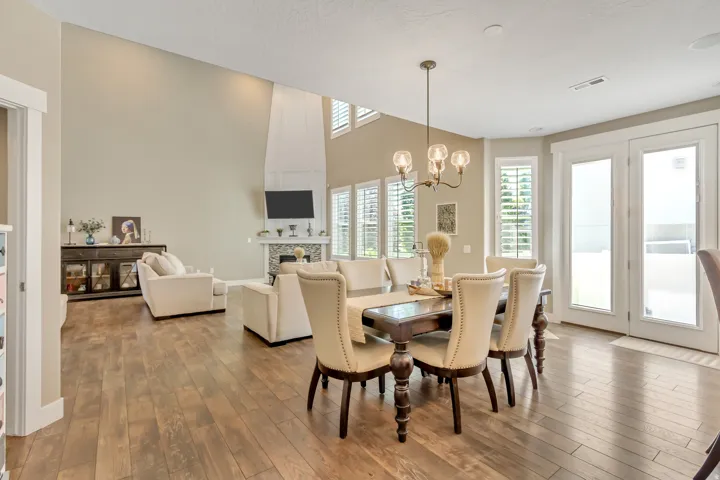 Spacious open-concept living area featuring wood-finish flooring, a dining area with an overhead chandelier, and a living room with a fireplace