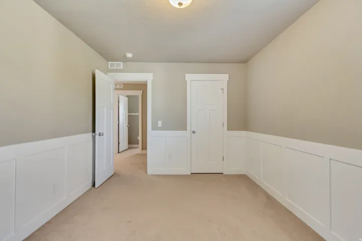 Neutral-toned room featuring wainscoting, plush carpet flooring, a flush-mount ceiling light, and white paneled doors with chrome hardware