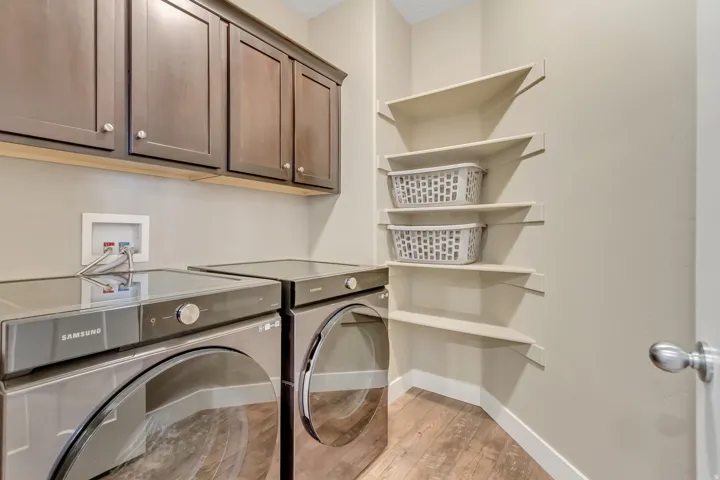 Dedicated laundry space featuring rich wood-finish upper cabinetry, a utility hookup, corner shelving, and wood-finish flooring