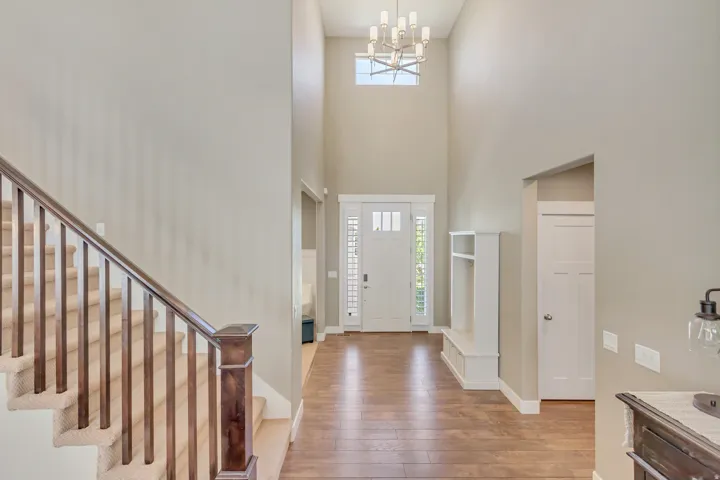 Entryway featuring soaring ceilings, wood-finish flooring, a built-in bench with storage, a contemporary chandelier, and a staircase with wood newel posts and carpeted treads