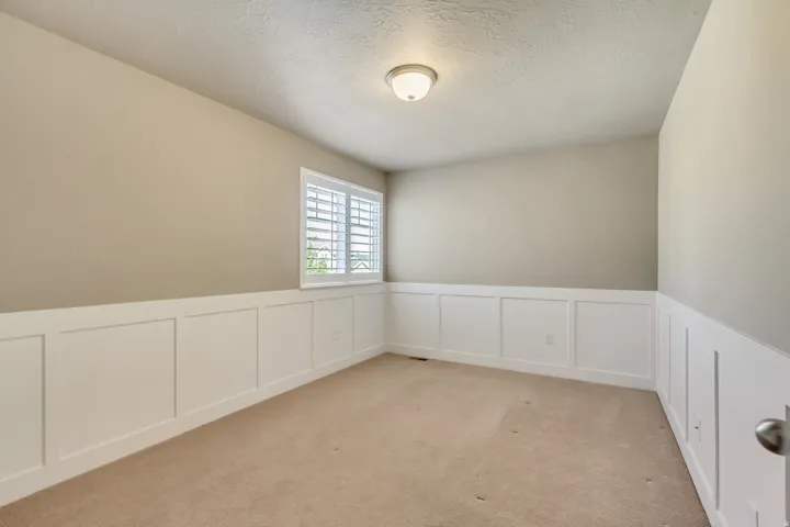 Interior room featuring neutral wall paint, white board and batten wainscoting, and a single window with white plantation shutters