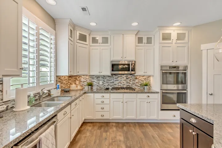 Kitchen featuring white shaker-style cabinetry, stainless steel appliances, granite countertops, wood-finish flooring, and a mosaic tile backsplash