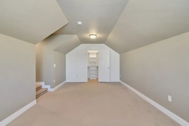 Carpeted attic space with sloped ceilings and recessed shelving behind a white door