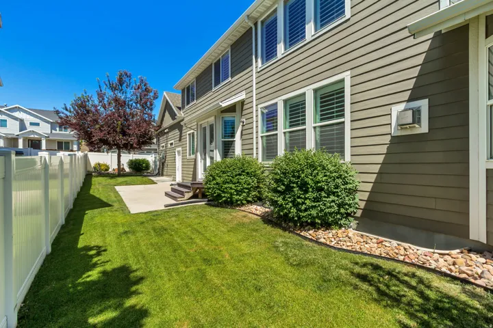 Expansive side yard featuring a manicured lawn, concrete patio, and mature landscaping