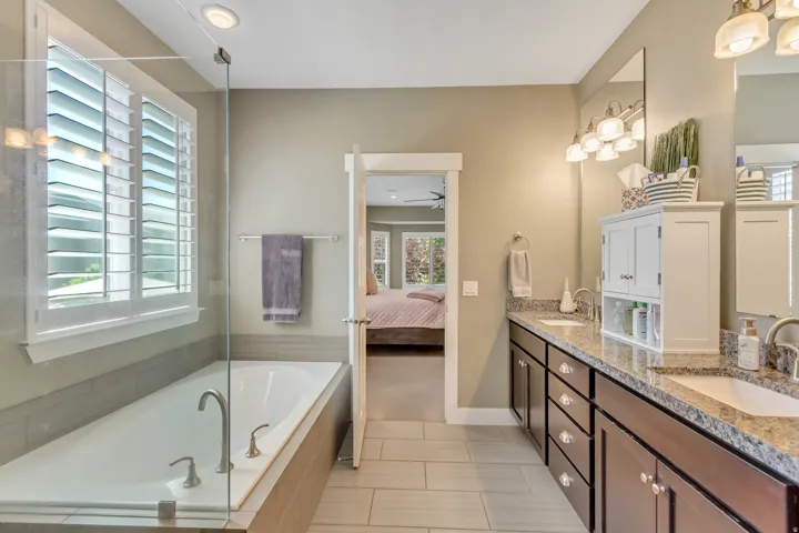 Bathroom featuring an elongated soaking tub with chrome fixtures, a clear glass shower enclosure, and white plantation shutters on the window
