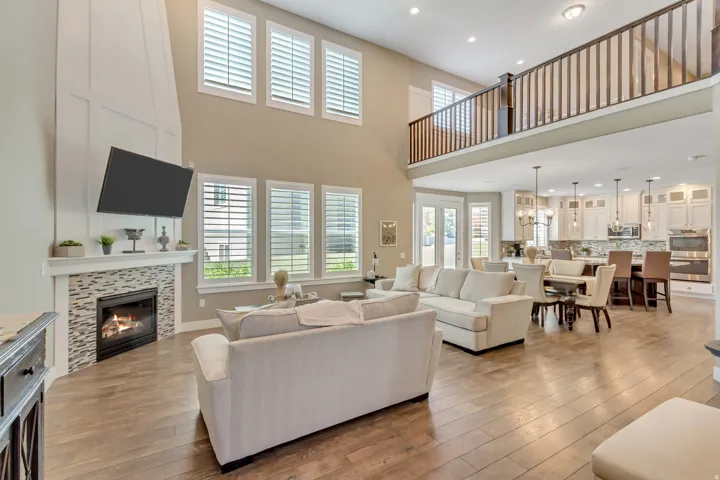 Spacious living area featuring high ceilings, wood-finish flooring, a contemporary fireplace with a tile surround, and multiple windows with plantation shutters