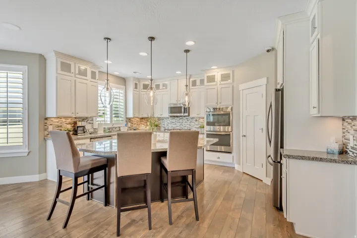 Open-concept kitchen featuring light-toned cabinetry, a multi-tone tile backsplash, and a central island with a stone countertop