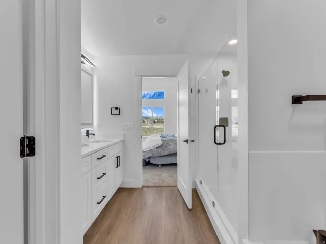 Modern bathroom with wood-finish flooring, white vanity with quartz countertop, and a glass-enclosed shower