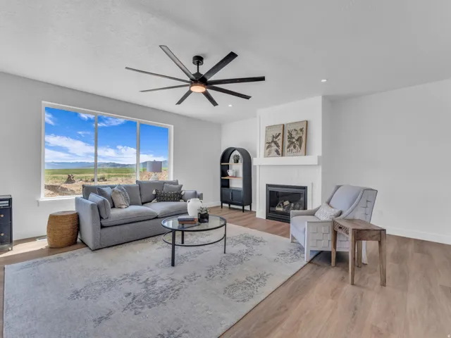Spacious living area featuring large picture windows, wood-finish flooring, a modern ceiling fan, a gas fireplace with a shiplap surround, and recessed lighting
