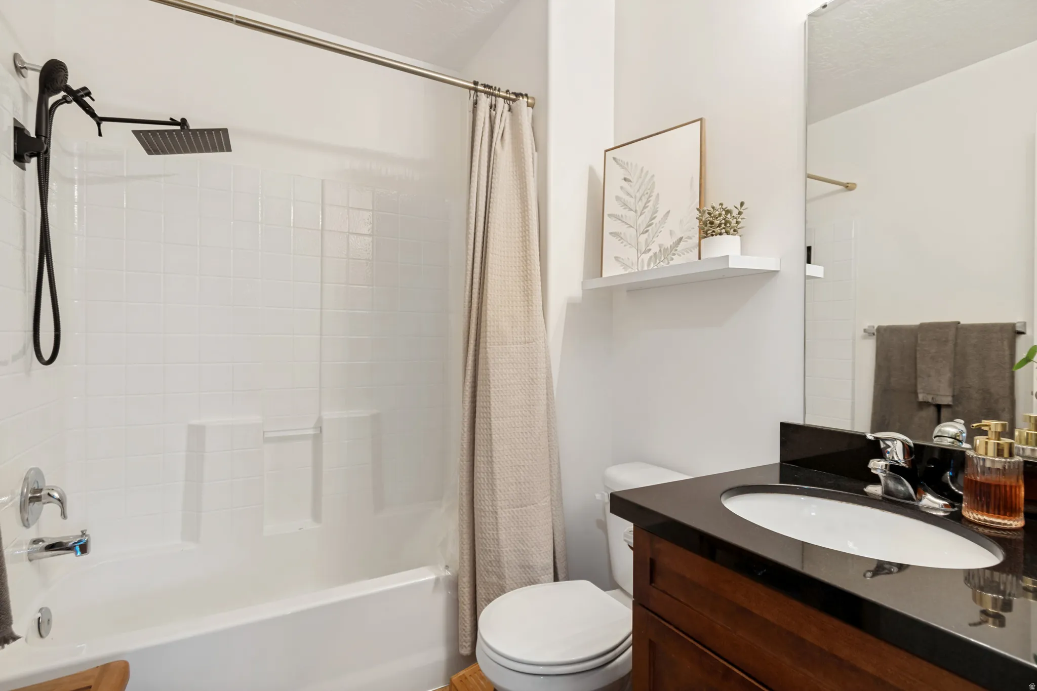 Bathroom featuring a white subway tile surround, a built-in tub, a black square rain shower head, a dark wood-finish vanity with a black countertop, and a white floating shelf