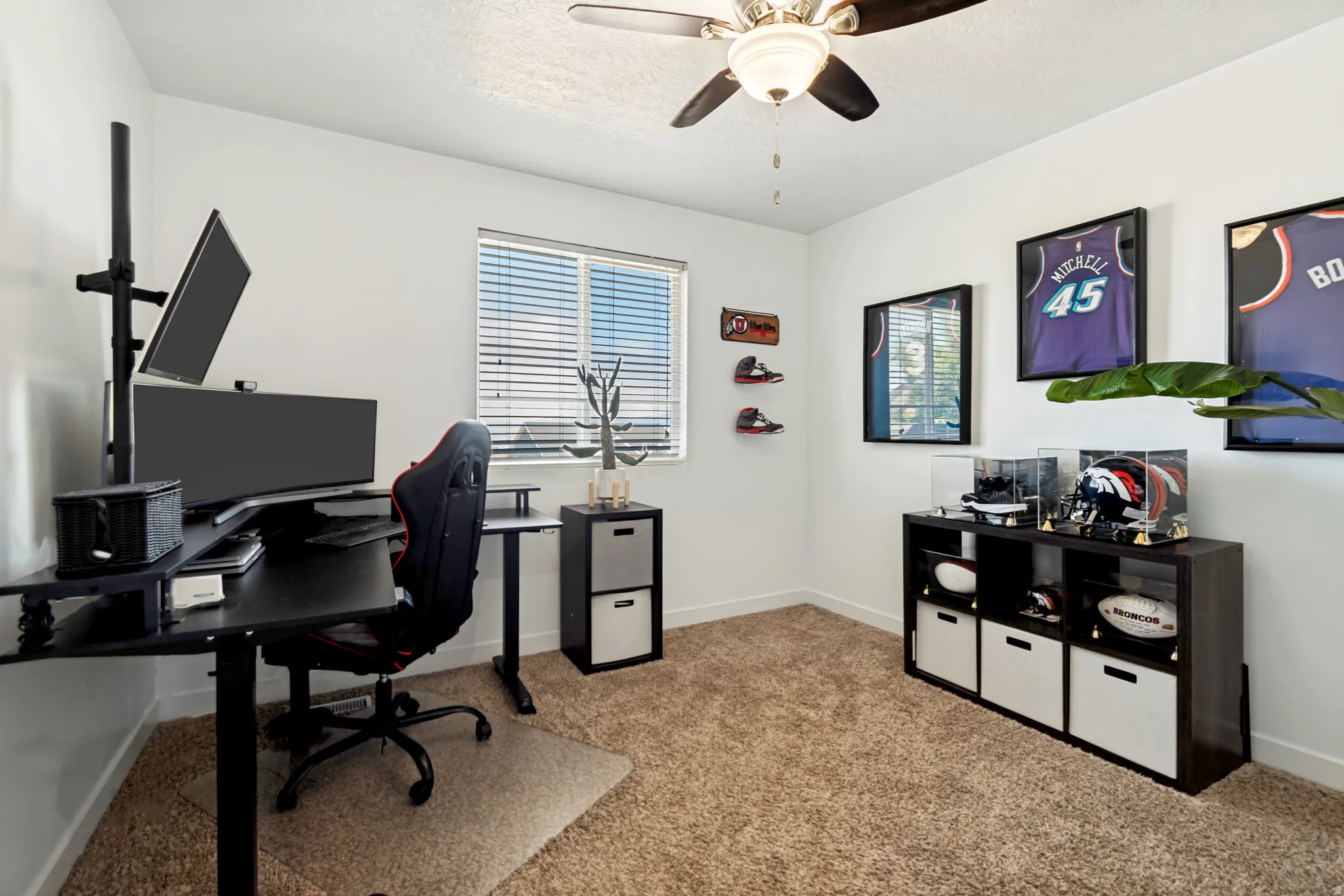 Carpeted room featuring a ceiling fan with integrated lighting, a window with horizontal blinds, and a built-in shelving unit