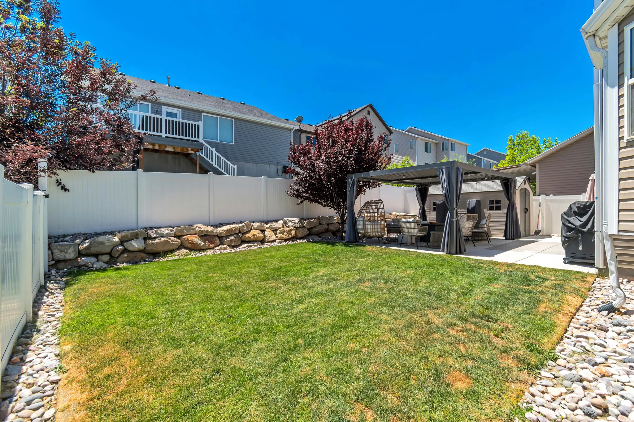 Expansive backyard featuring a lush lawn, a stone retaining wall, and a white privacy fence