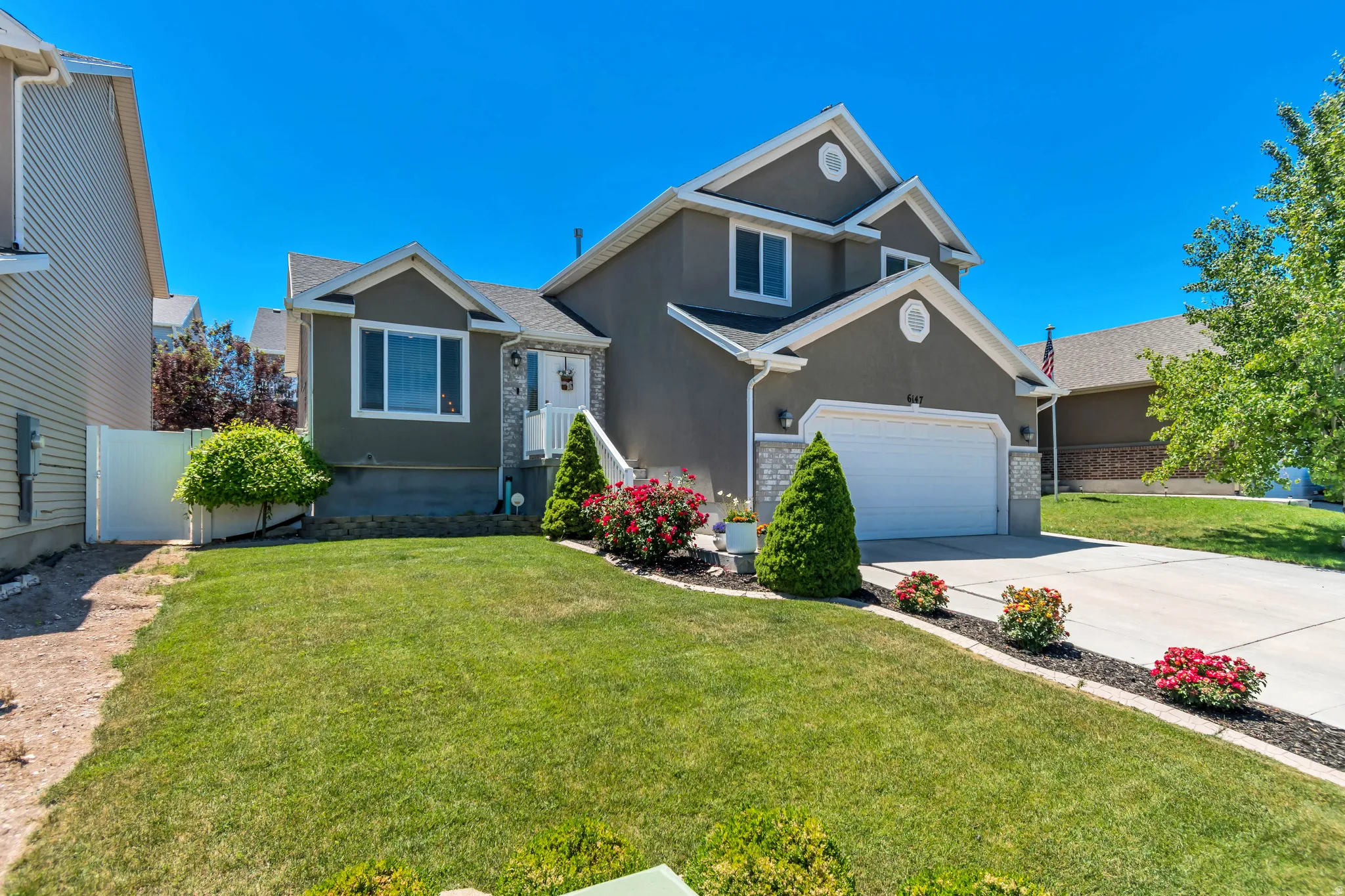 Two-story stucco exterior featuring a prominent gabled roofline, stone facade accents, and a two-car garage
