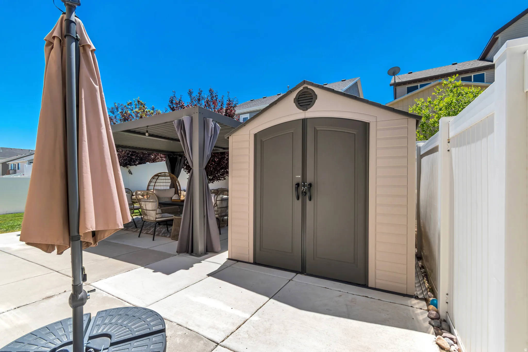 Concrete patio area featuring a detached storage shed, a white privacy fence, and a gazebo with drapes