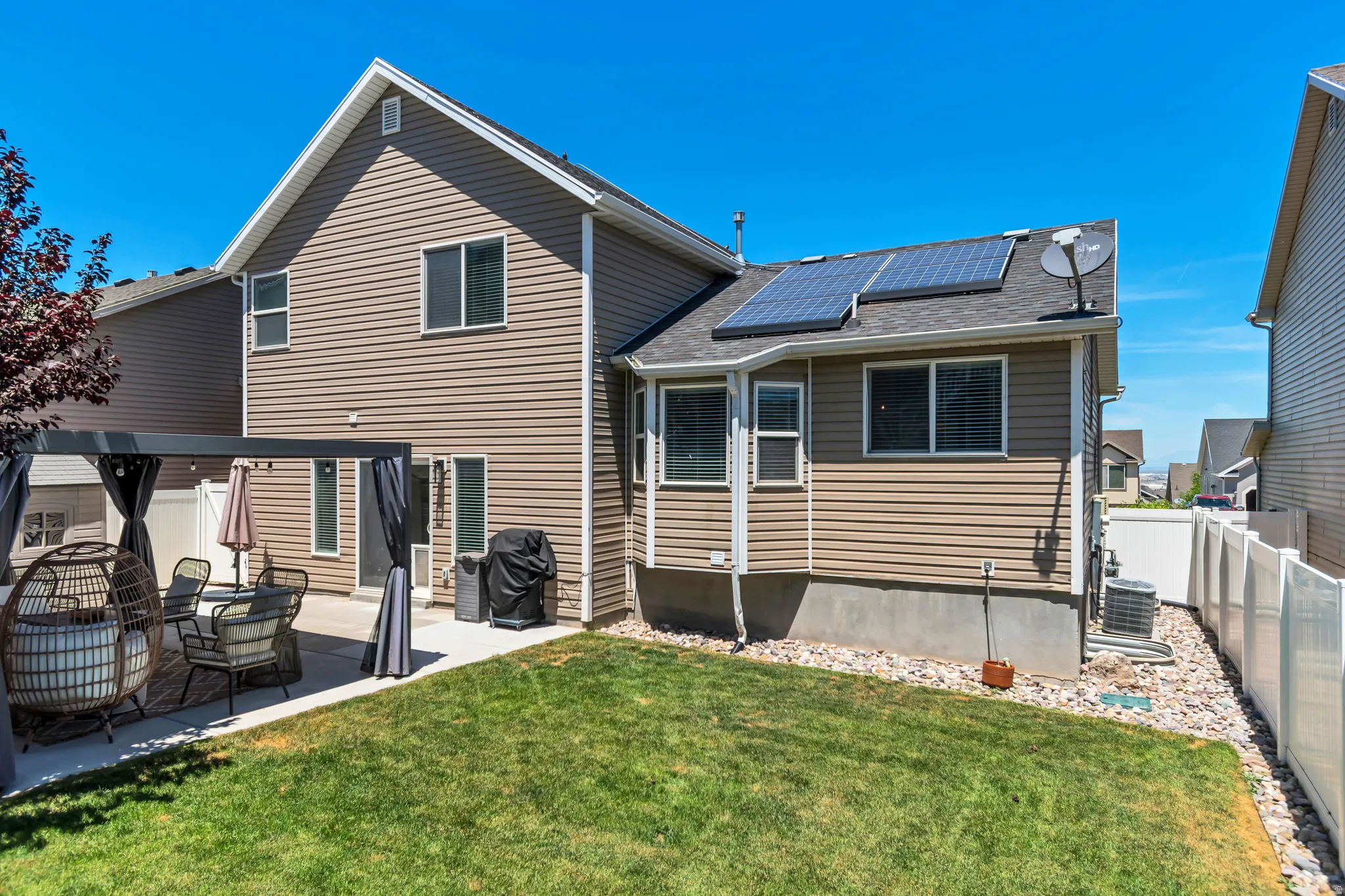 Rear exterior featuring tan siding, a concrete patio, and an expanse of green lawn