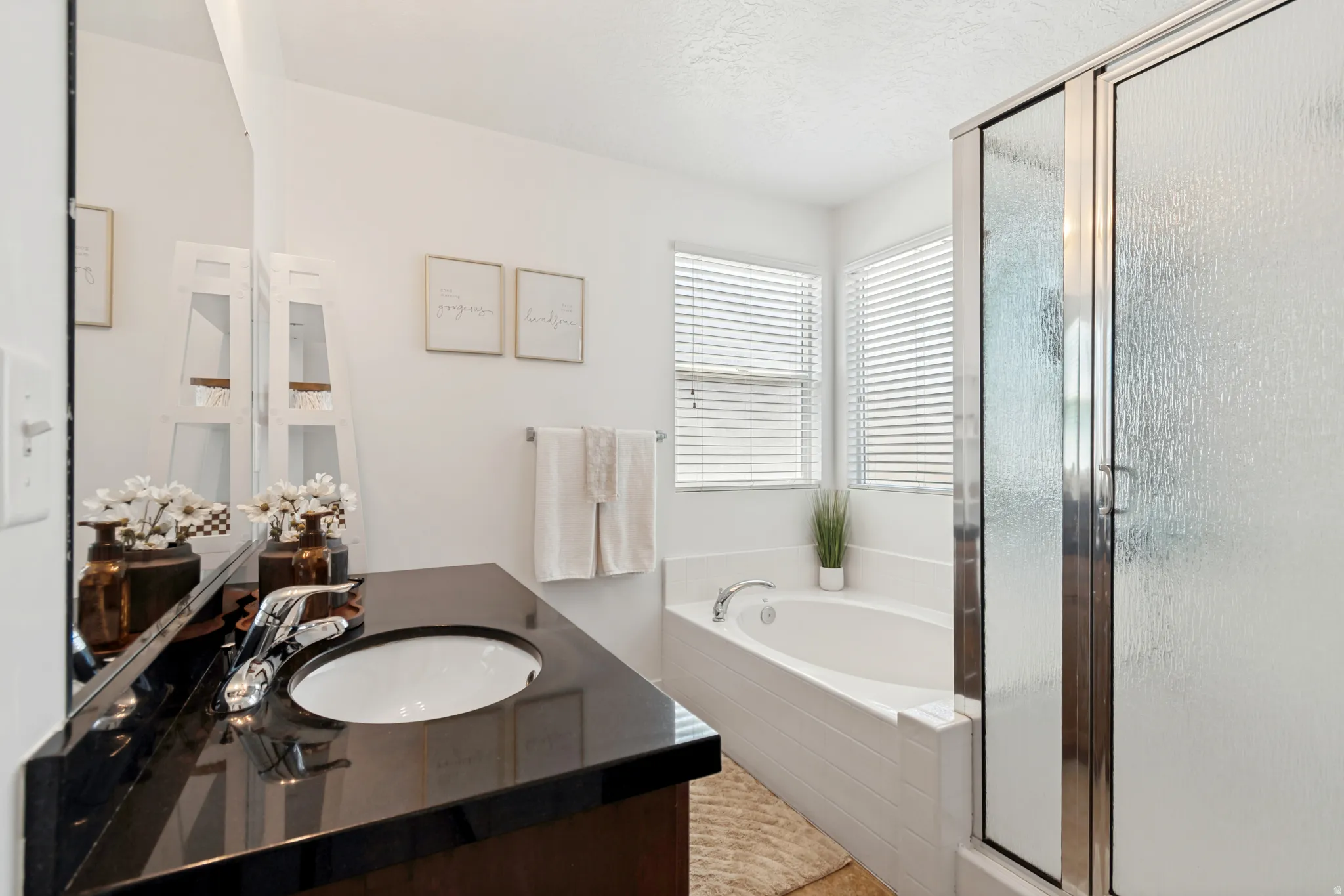 Bathroom featuring a black countertop with an integrated sink, a built-in bathtub, and an enclosed shower with textured glass
