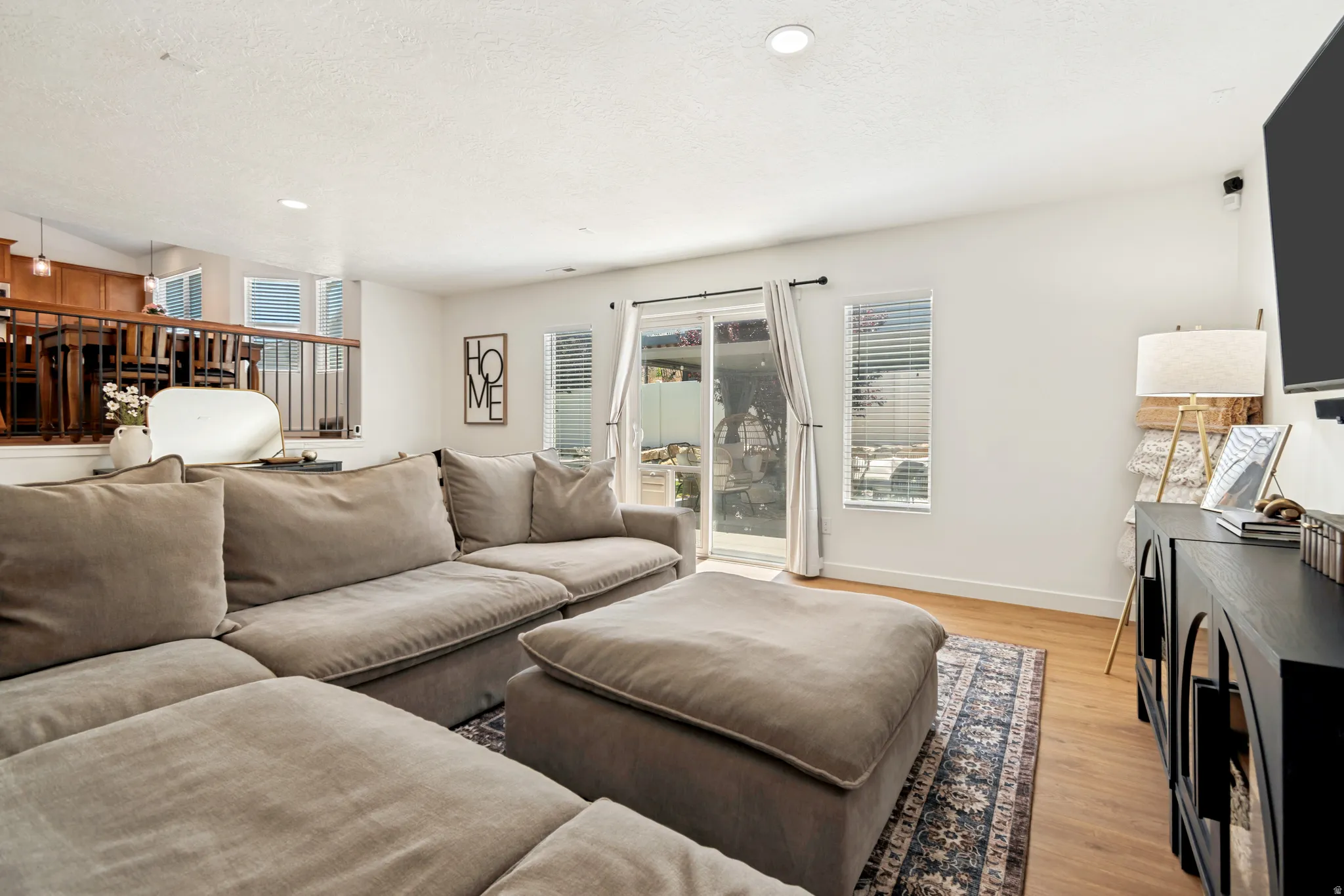 Living area featuring wood-finish flooring, recessed lighting, white walls, a sliding glass door, and an interior balcony with wood railing