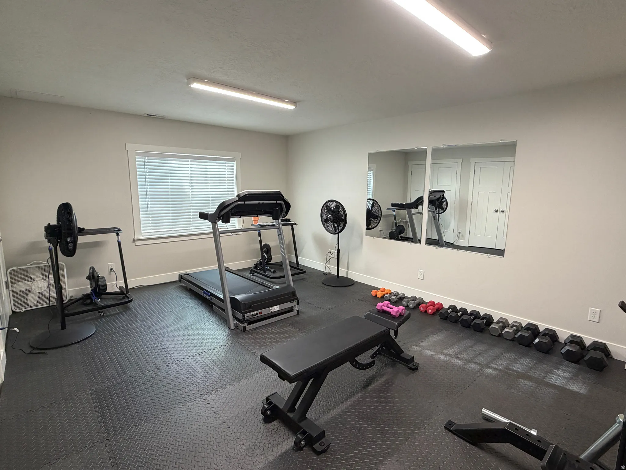 Flexible-use room featuring a window with blinds, wall-mounted mirrors, recessed lighting, and durable rubber flooring