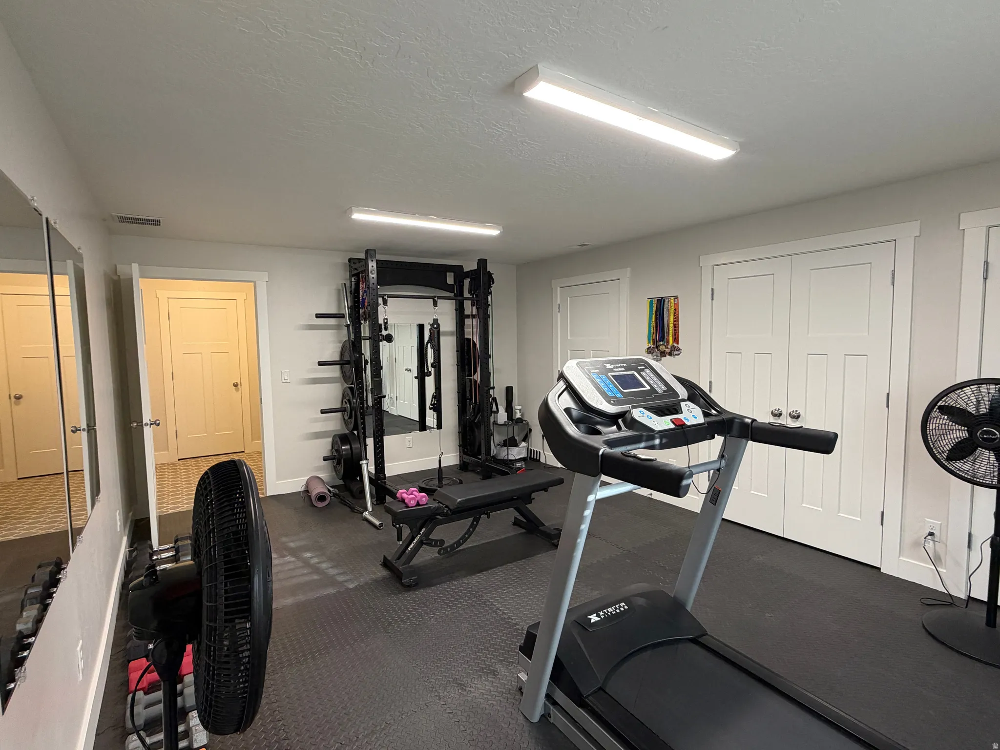 Dedicated fitness space featuring rubber mat flooring, overhead strip lighting, white baseboards, and two paneled closet doors