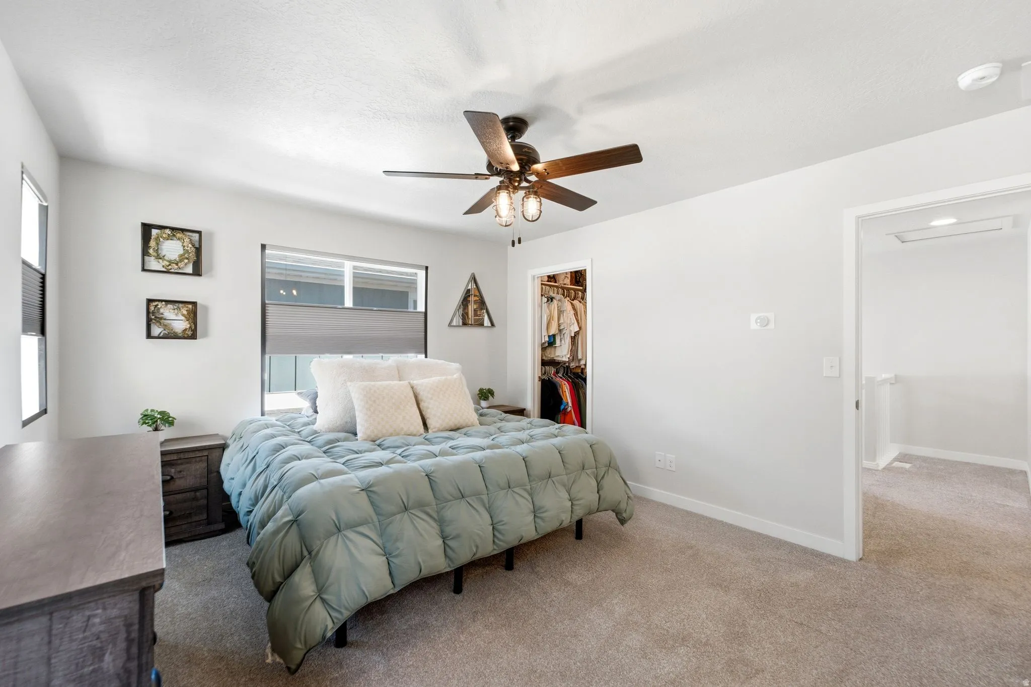 Carpeted bedroom featuring a ceiling fan with integrated lighting, multiple windows with blinds, a walk-in closet, and neutral wall finishes