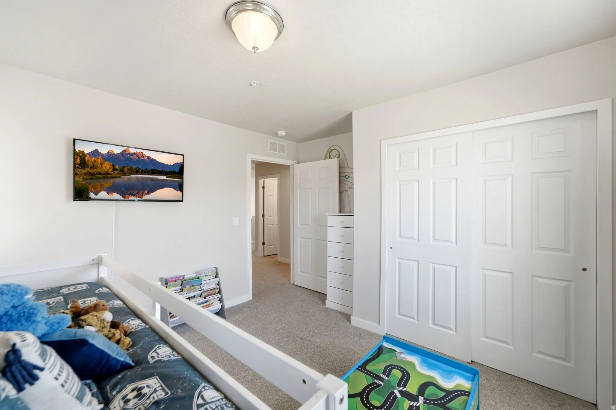 Carpeted room featuring light gray walls, a built-in closet with white bi-fold doors, a wall-mounted flat-screen television, and a flush-mount ceiling light fixture