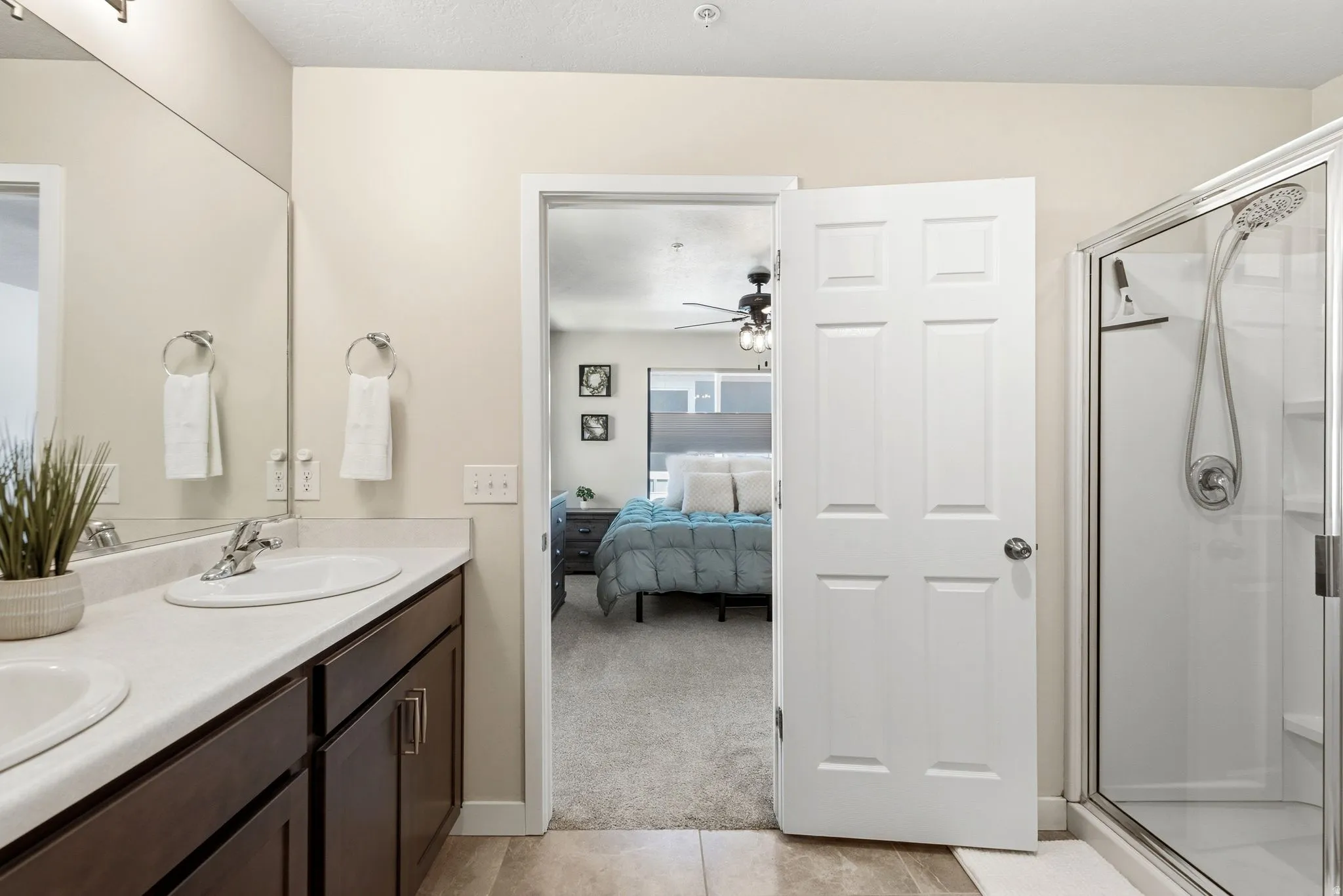 Bathroom featuring a double vanity with dark wood-finish cabinetry and light countertops, an integrated sink, and a glass-enclosed shower with a rainfall showerhead