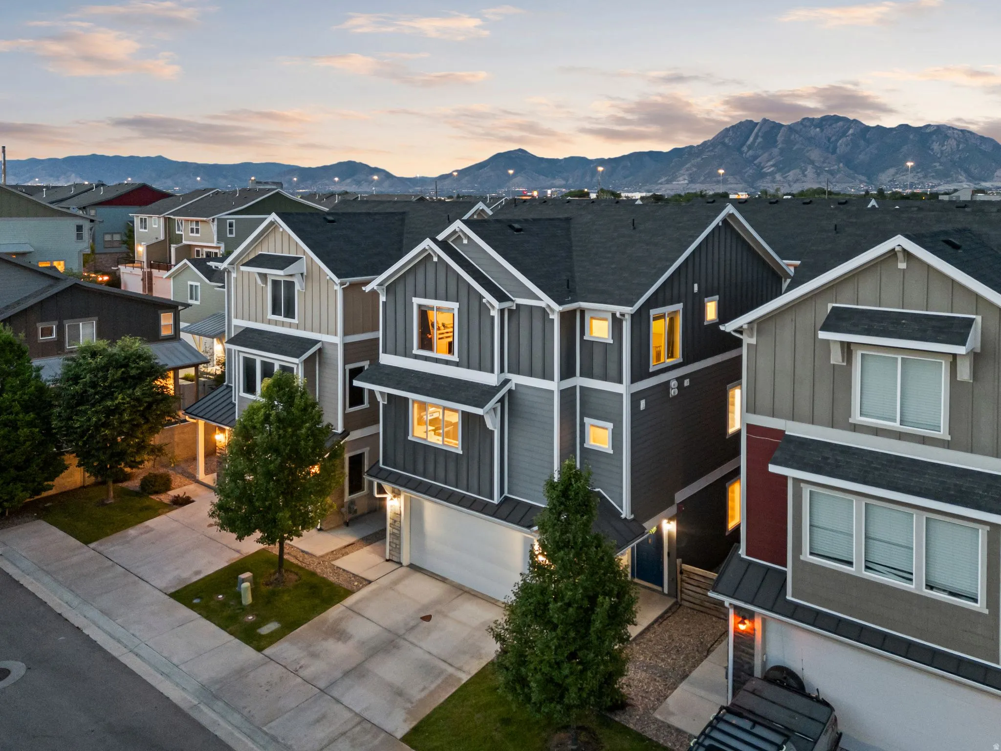 Contemporary multi-level townhome featuring a two-car garage, dark-pitched roof, horizontal and vertical siding, and a mountain backdrop