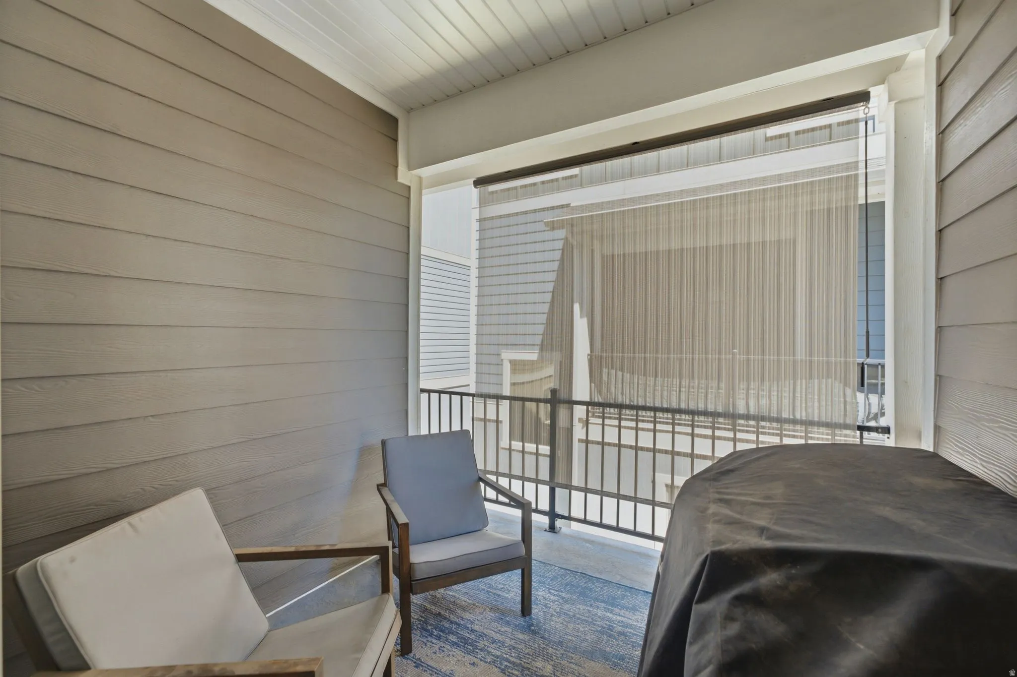 Covered outdoor patio featuring horizontal plank siding, a white tongue-and-groove ceiling, and a black metal railing