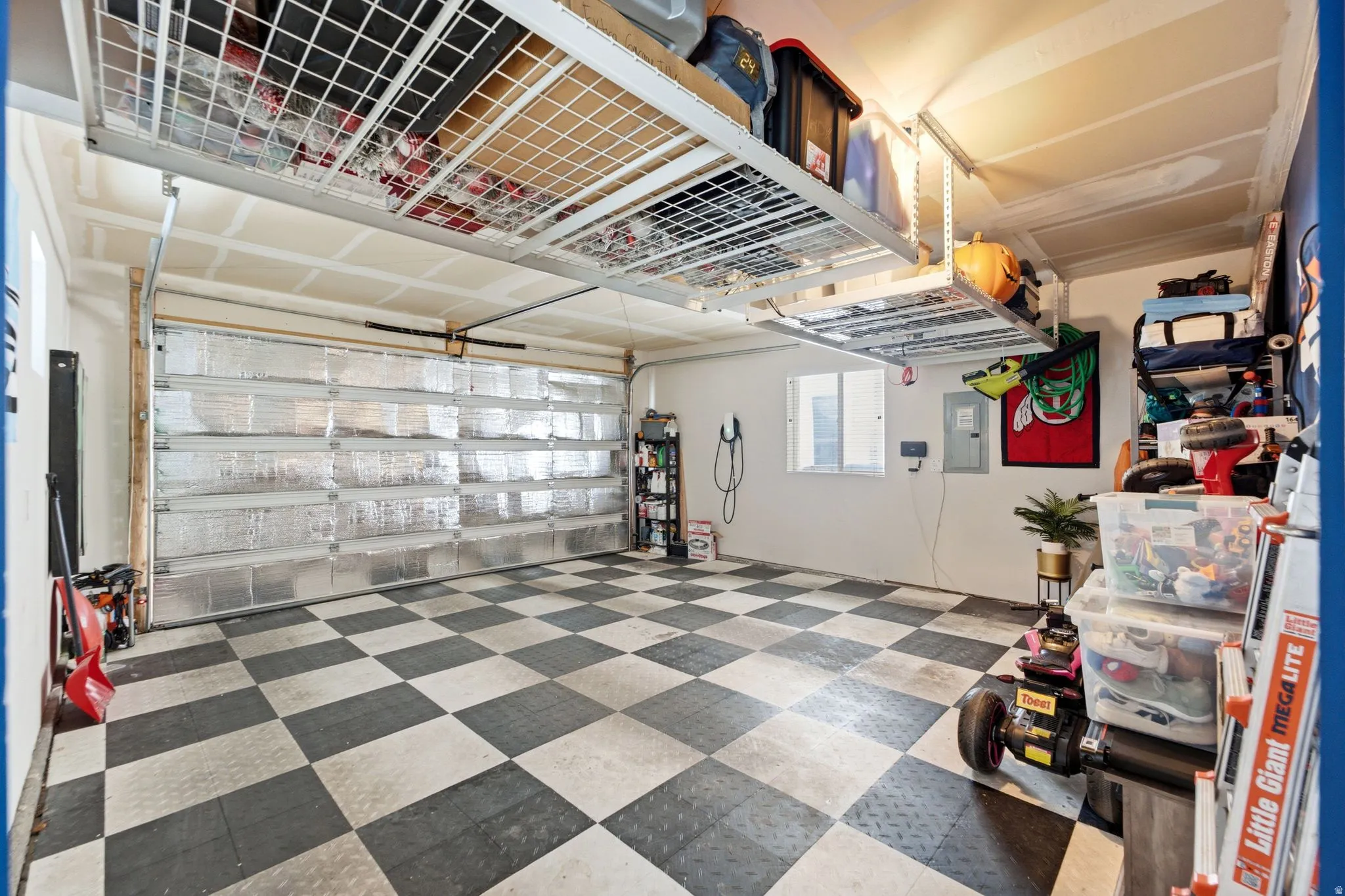 Garage featuring checkerboard flooring, overhead storage racks, and an insulated garage door