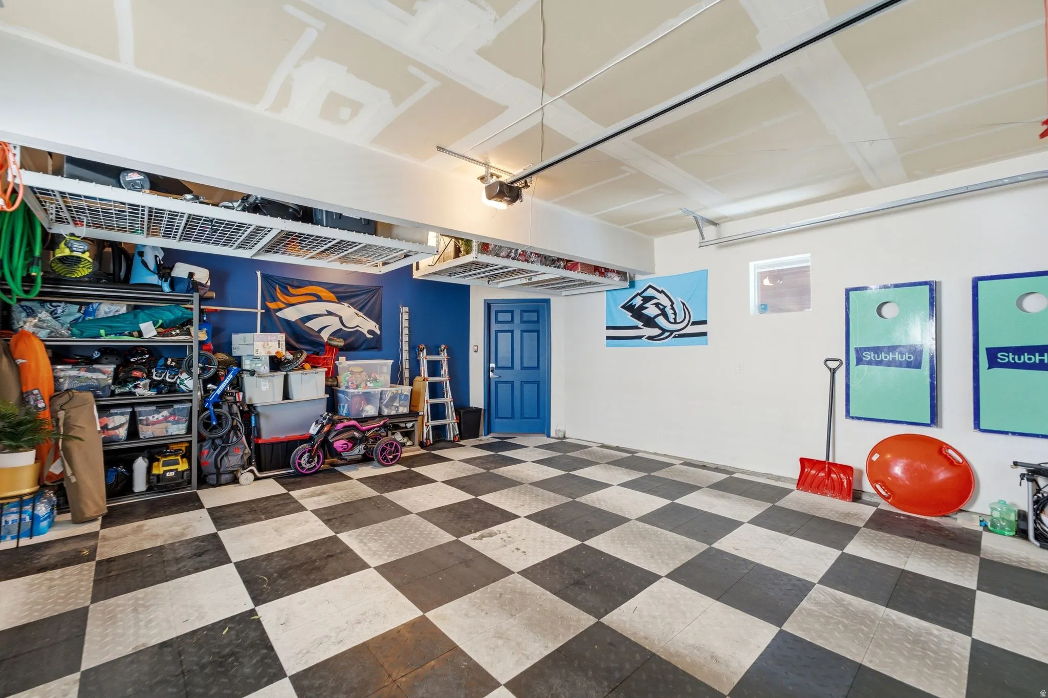 Spacious garage featuring checkerboard flooring, overhead storage racks, a side-entry door, and a high ceiling