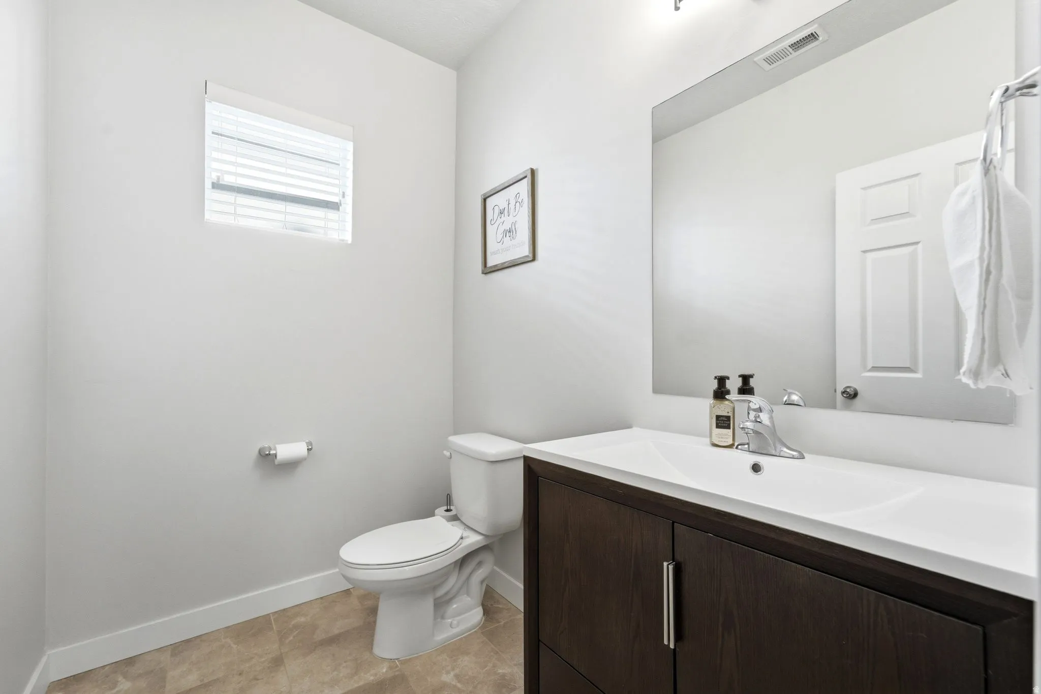 Bathroom featuring a dark wood-finish vanity with an integrated white sink, a large wall-mounted mirror, and tile flooring