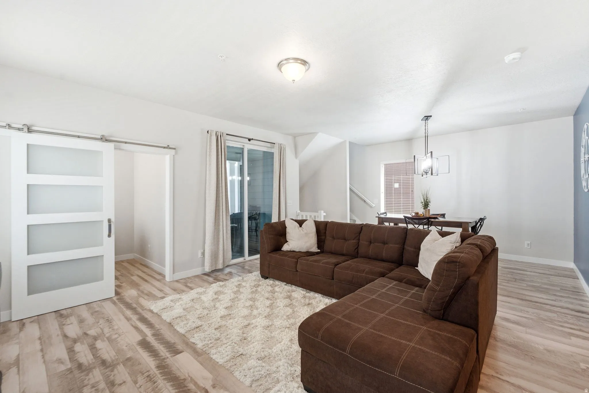 Open-concept living area featuring wood-finish flooring, a contemporary ceiling light fixture, and a sliding barn door with frosted glass panels