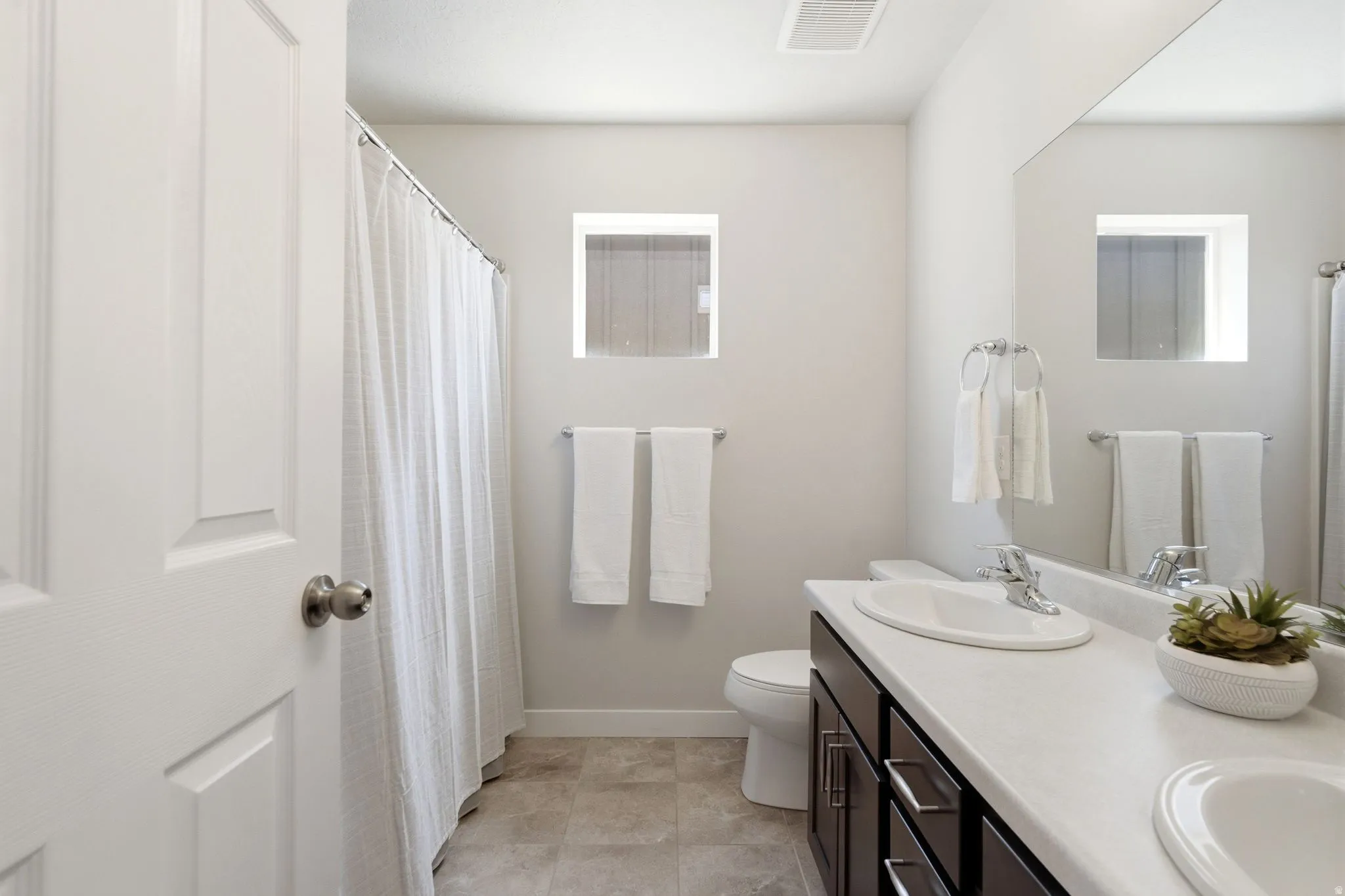 Bathroom featuring a dark wood-finish vanity with dual sinks, a spacious countertop, and a large mirror